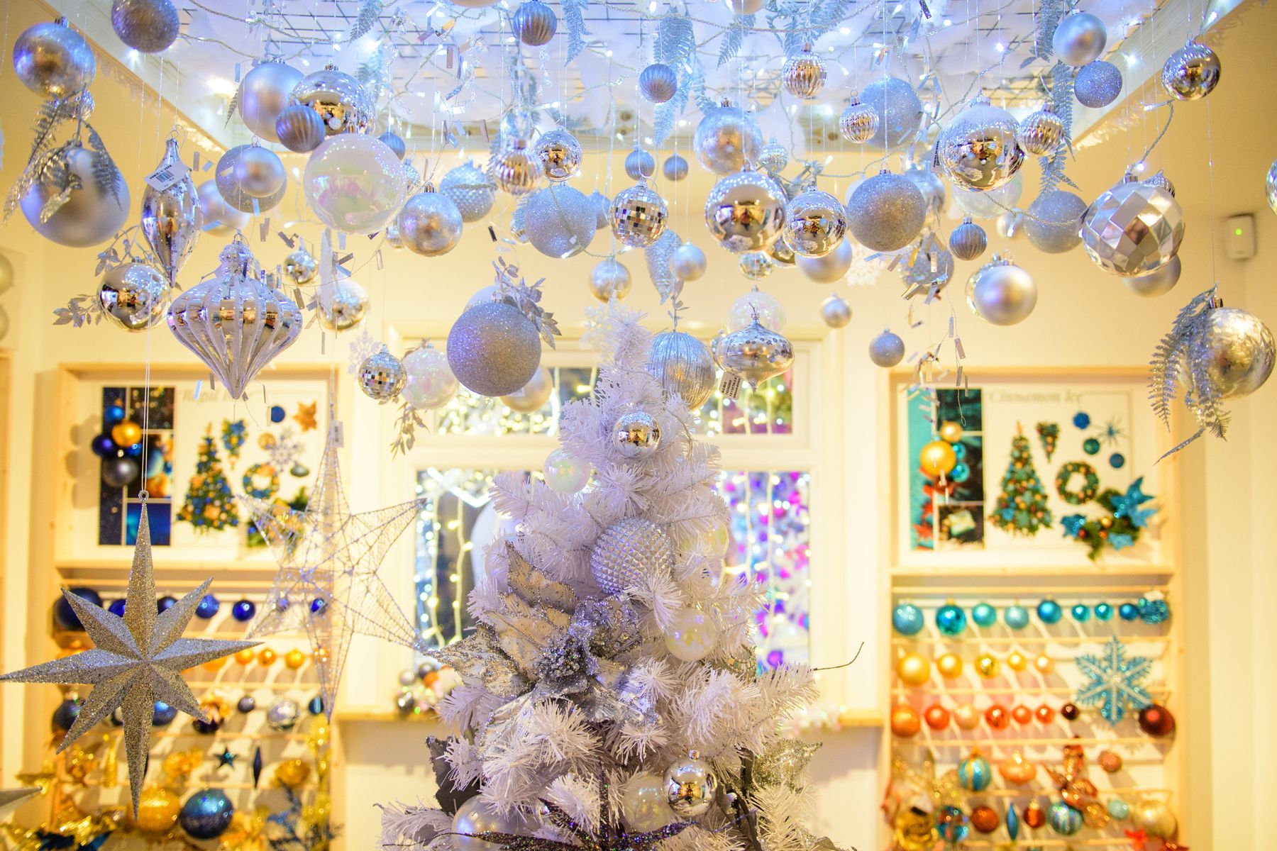 A white christmas tree is sitting under a ceiling covered in christmas decorations.