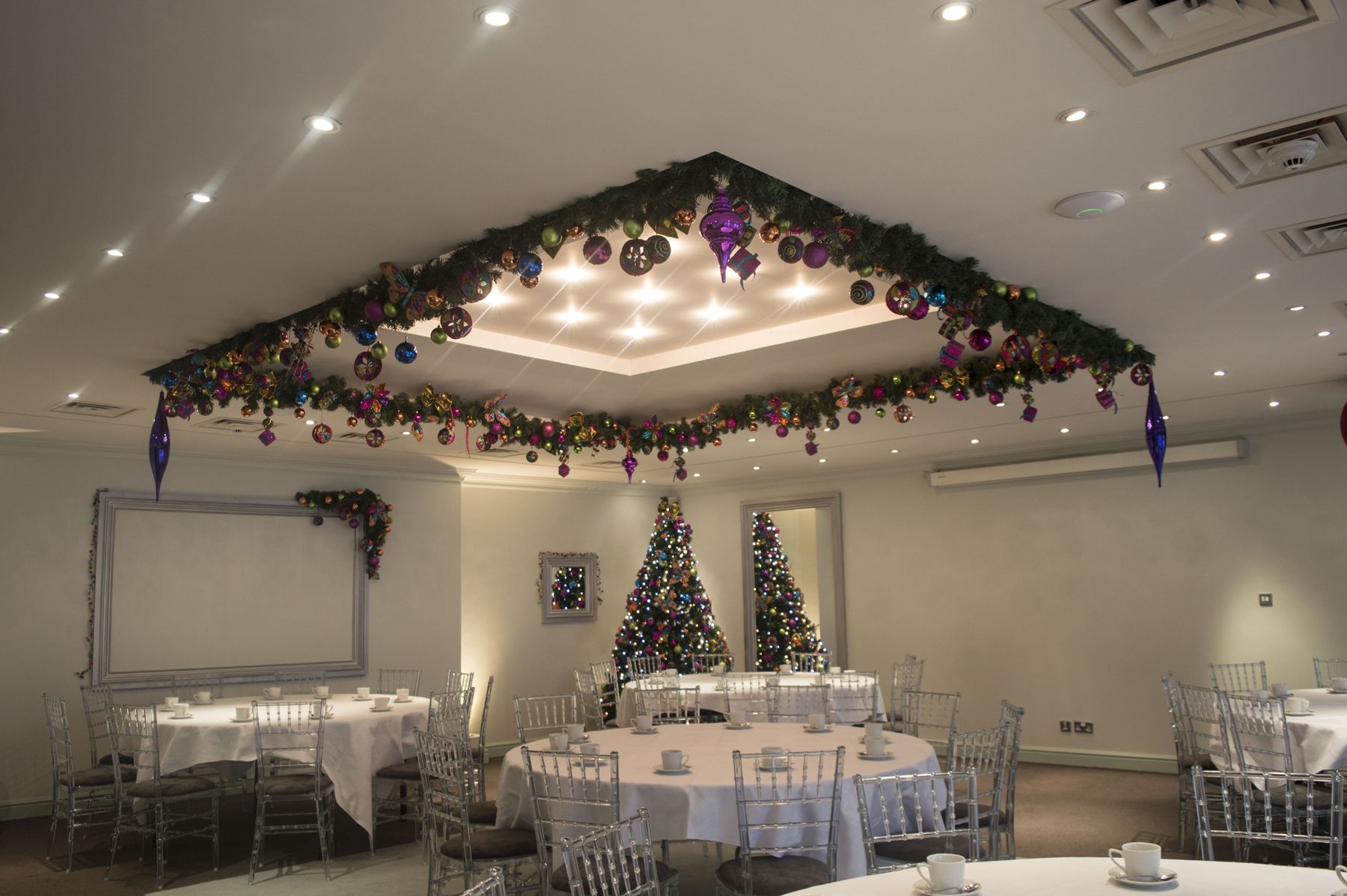 A large room with tables and chairs and christmas decorations on the ceiling.