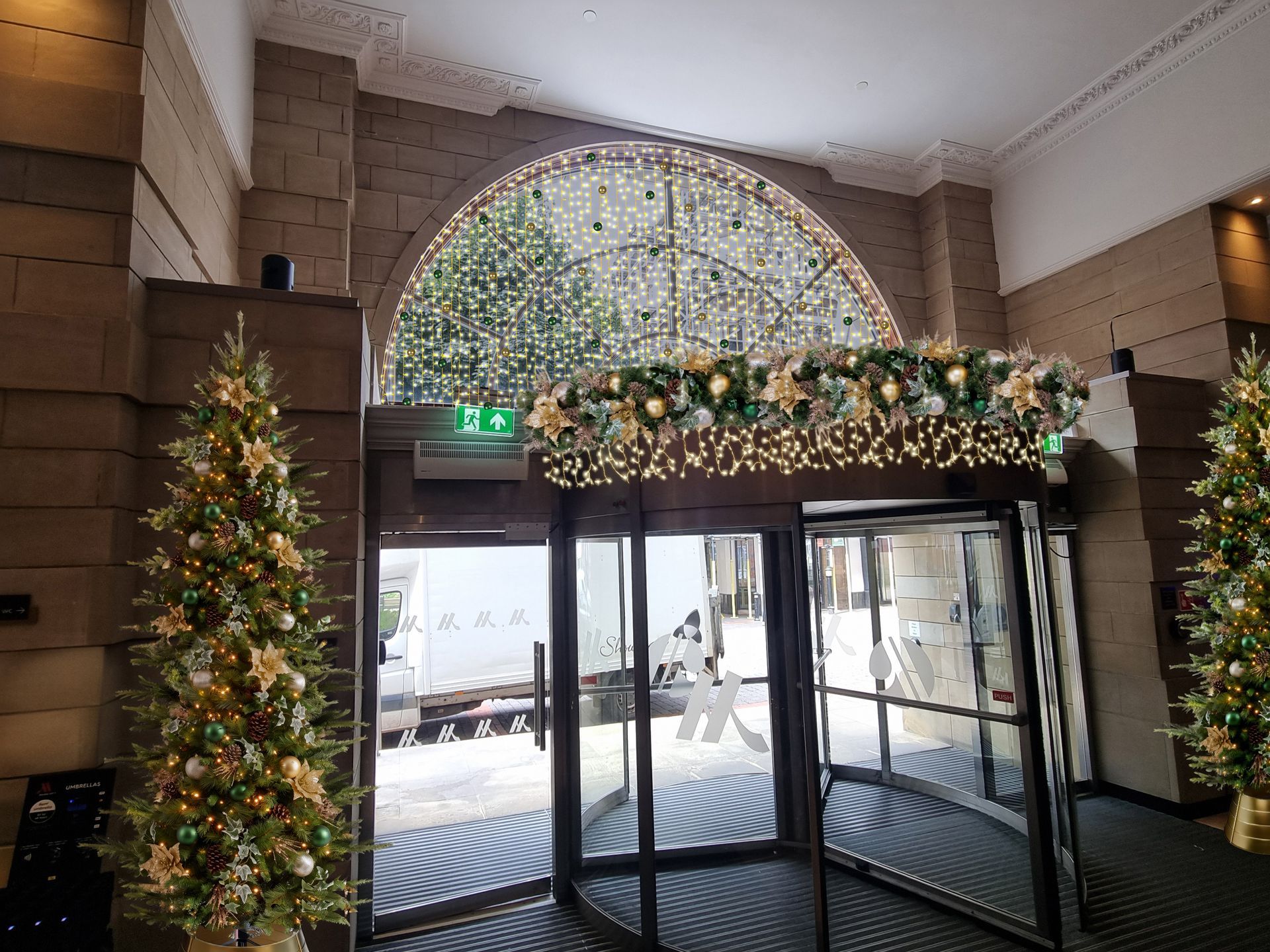 Decorated hotel entrance with Christmas trees and wreaths under an arched glass canopy