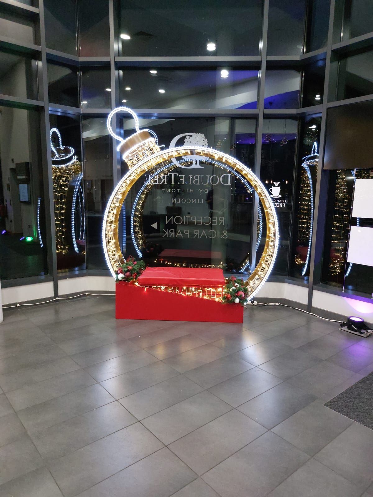 Holiday light display shaped like a giant ornament in a glass lobby with a red base