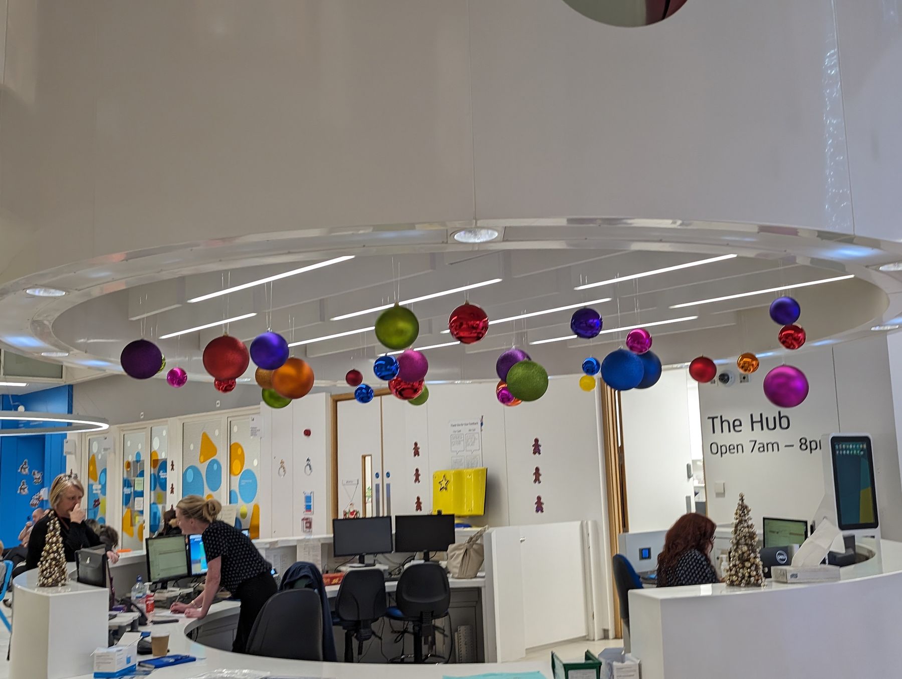 A woman is standing at a desk in an office with christmas decorations hanging from the ceiling.