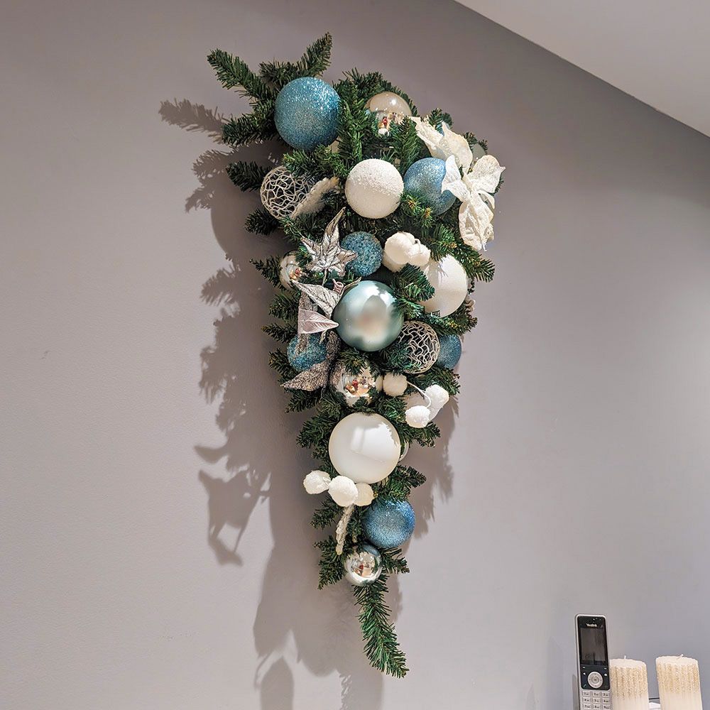 A christmas wreath with blue and white ornaments is hanging on a wall.