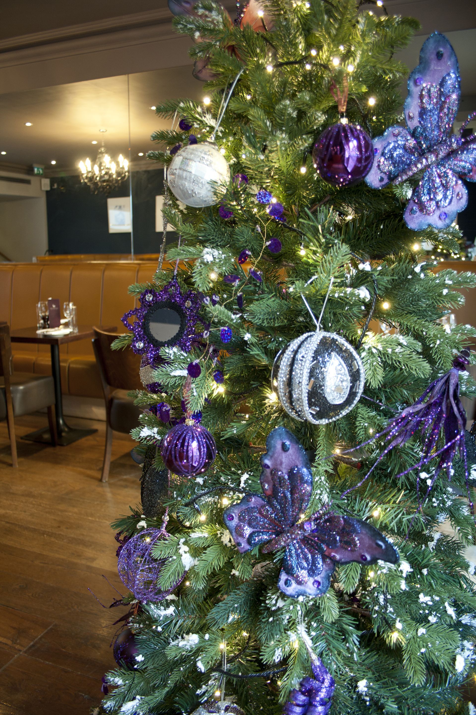 A christmas tree decorated with purple and silver ornaments in a restaurant.
