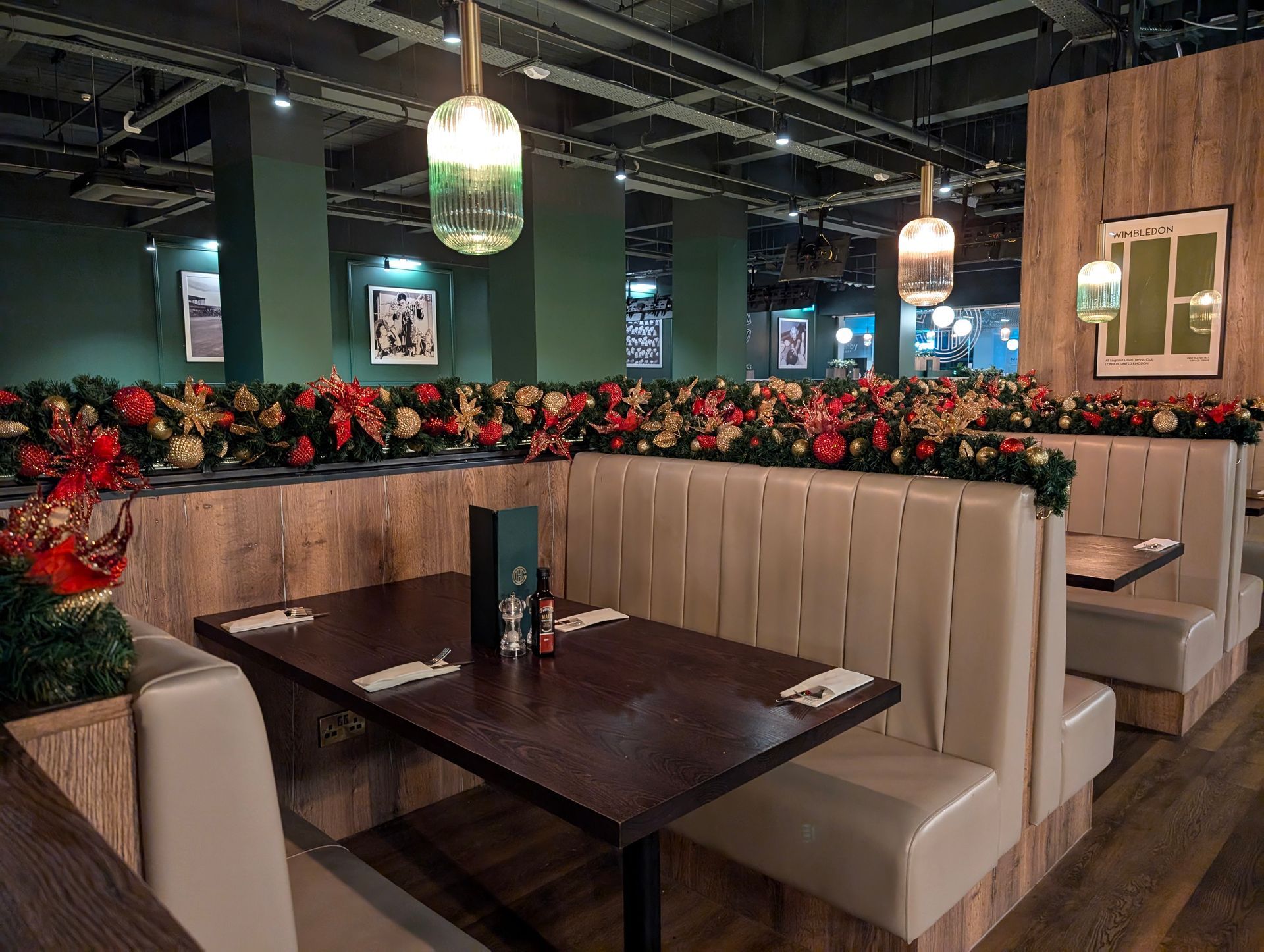 Booth seating in a dim restaurant with dark wood tables, green walls, and hanging pendant lights