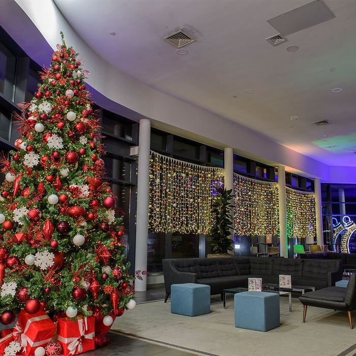 Decorated Christmas tree in a modern lounge with red ornaments, gift boxes, and holiday lights