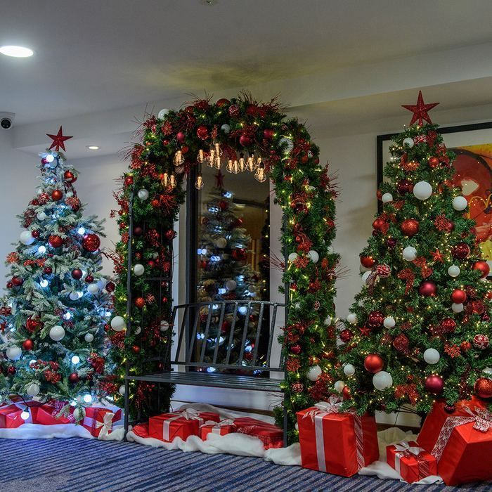 Living room with three decorated Christmas trees, garland-framed mirror, and wrapped gifts on the floor