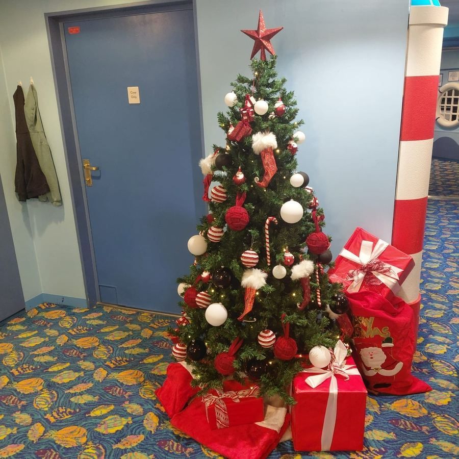 Christmas tree with red and white ornaments and wrapped gifts in a hallway.