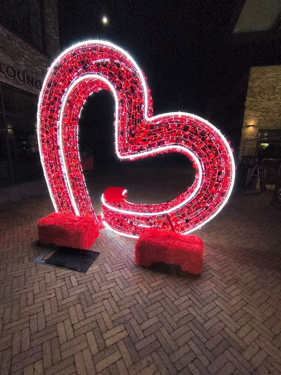 Neon heart-shaped light sculpture in red and white on a brick walkway at night