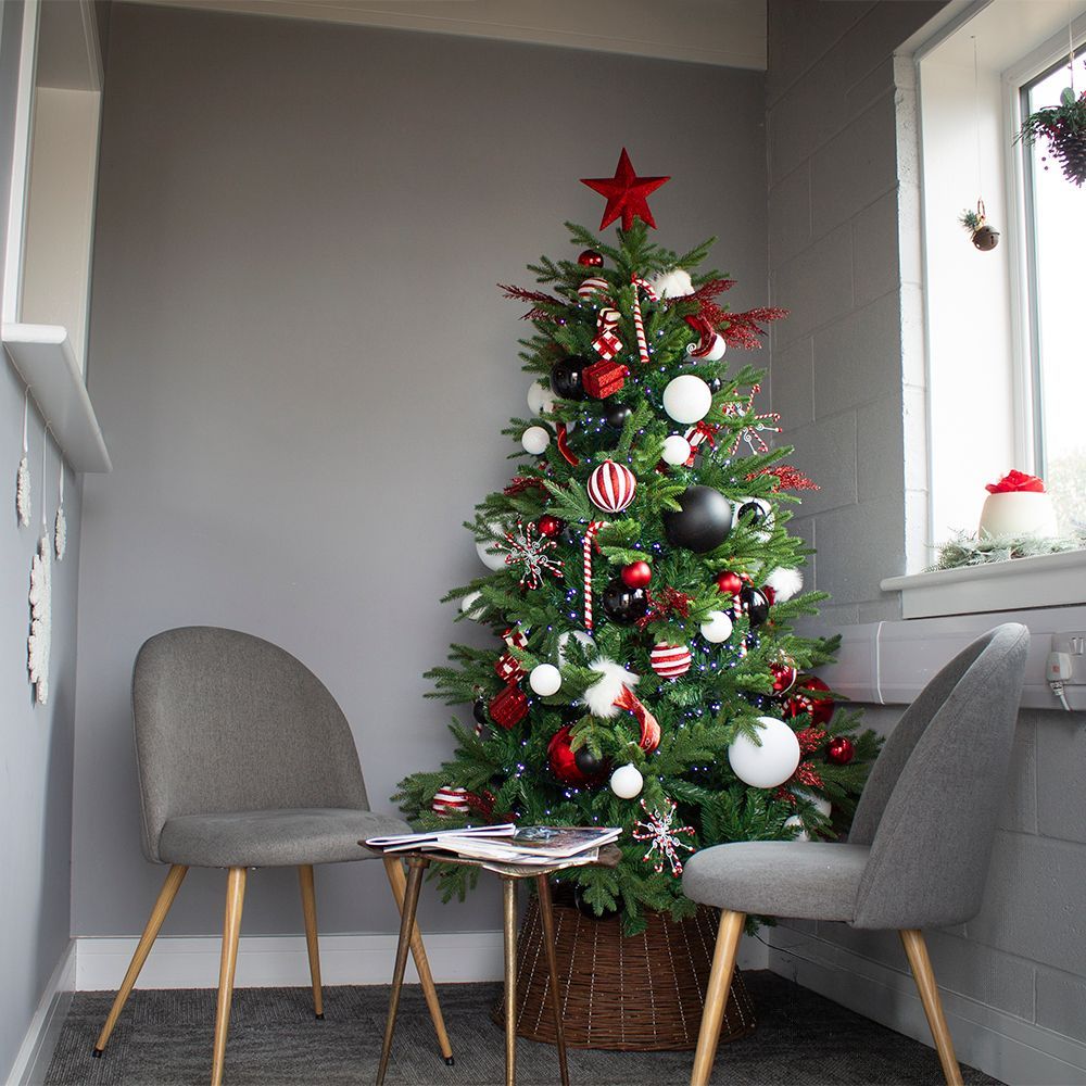 Cozy room with a decorated Christmas tree beside two gray chairs and a small table by a window.