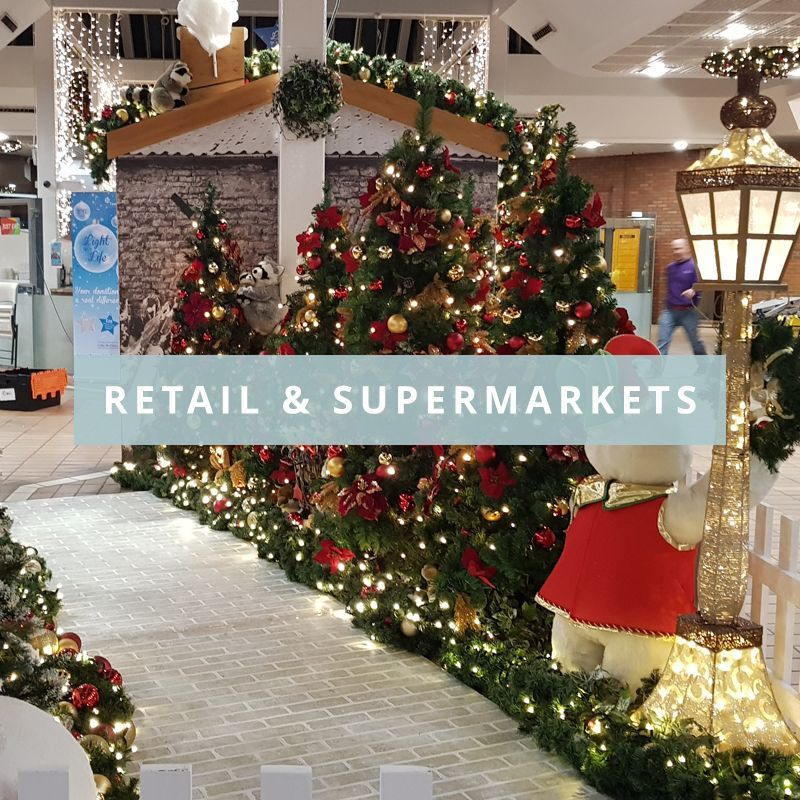 A row of christmas trees in a mall with the words retail & supermarkets above them.