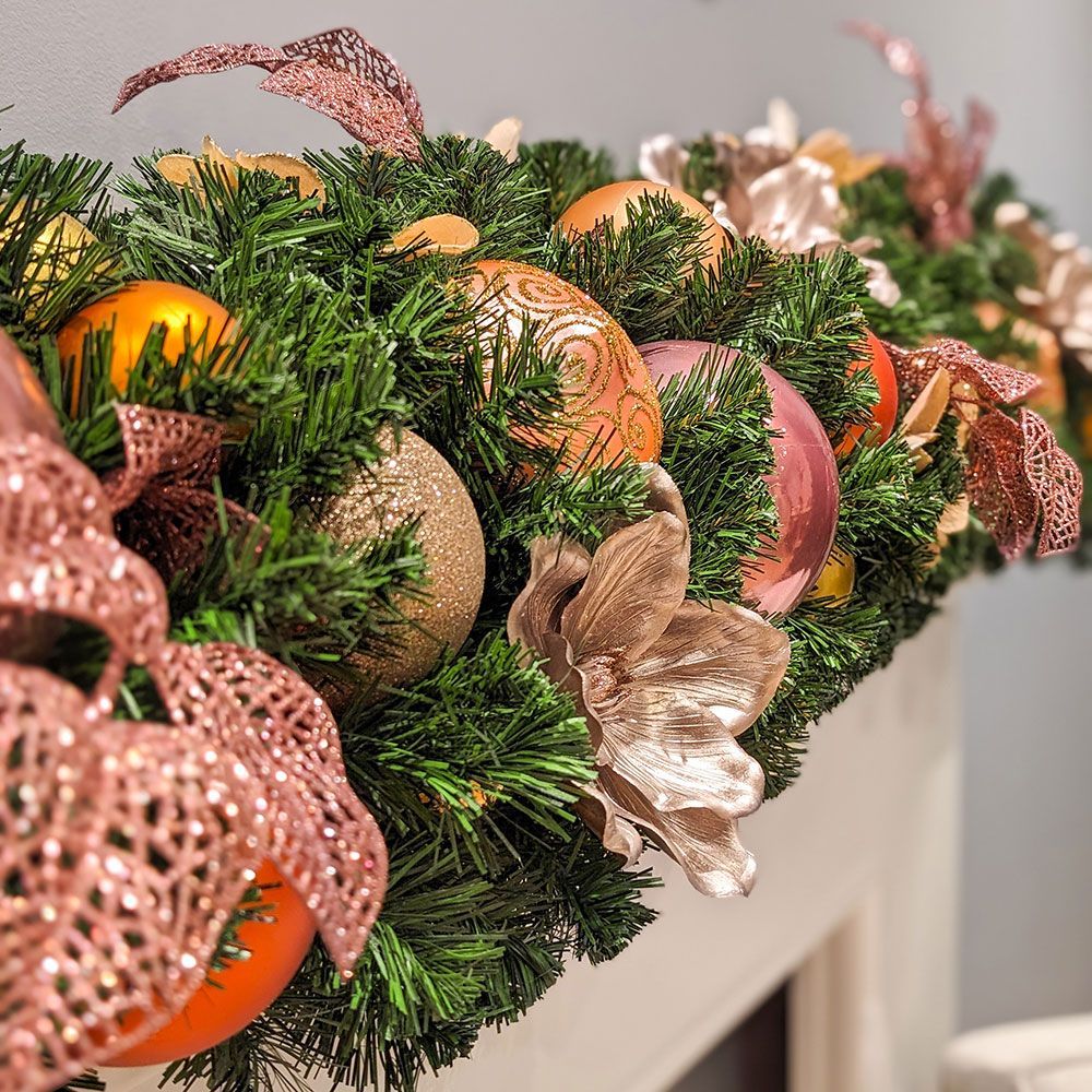 Decorated Christmas tree beside a wicker hanging chair in a cozy corner with a fireplace mantel.