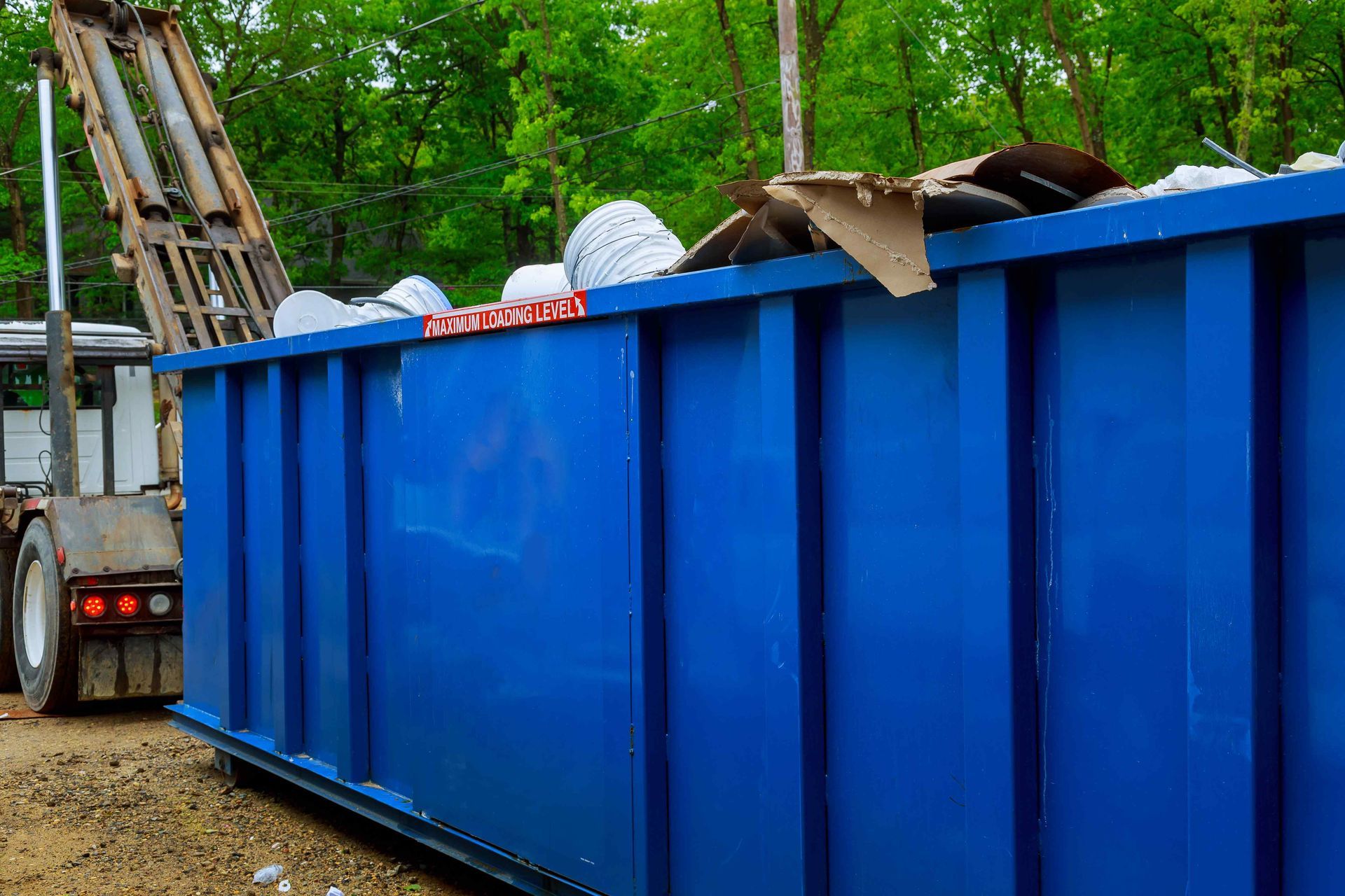 Yellow dumpster filled with debris on a city street, houses in the background.