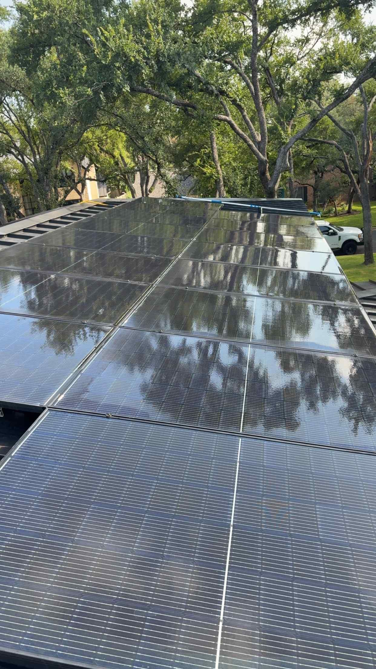 Solar panels on a roof covered in a thin layer of water, reflecting the surrounding trees and sky.