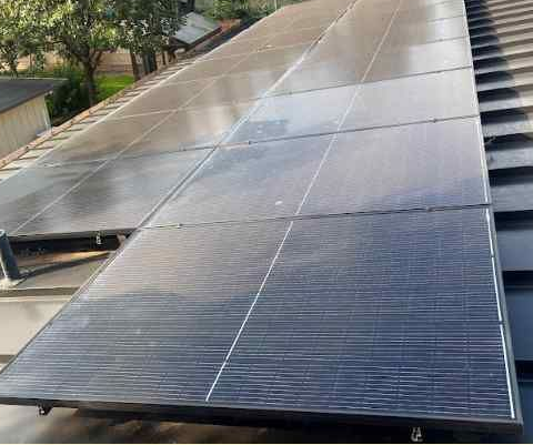Solar panels installed in a grid pattern on a dark sloped roof under a clear sky.