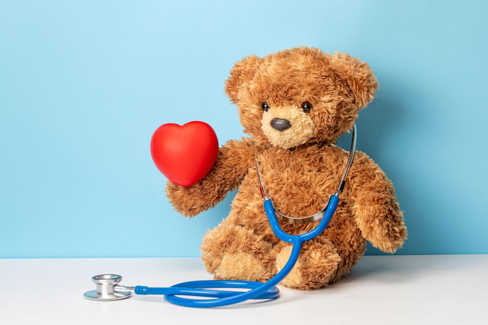 Teddy bear with blue stethoscope holding a heart.