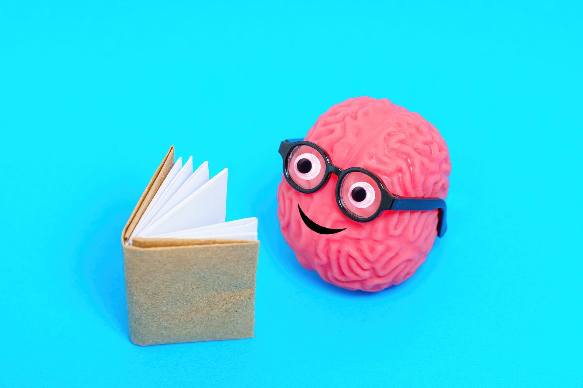 A cartoon brain wearing glasses is reading a book on a blue background.