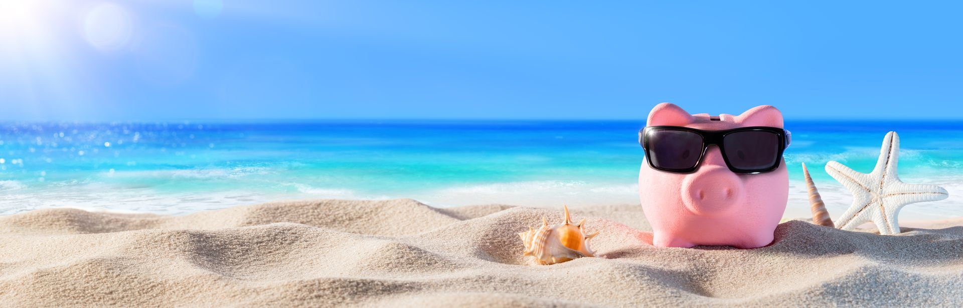 A piggy bank wearing sunglasses on the beach.