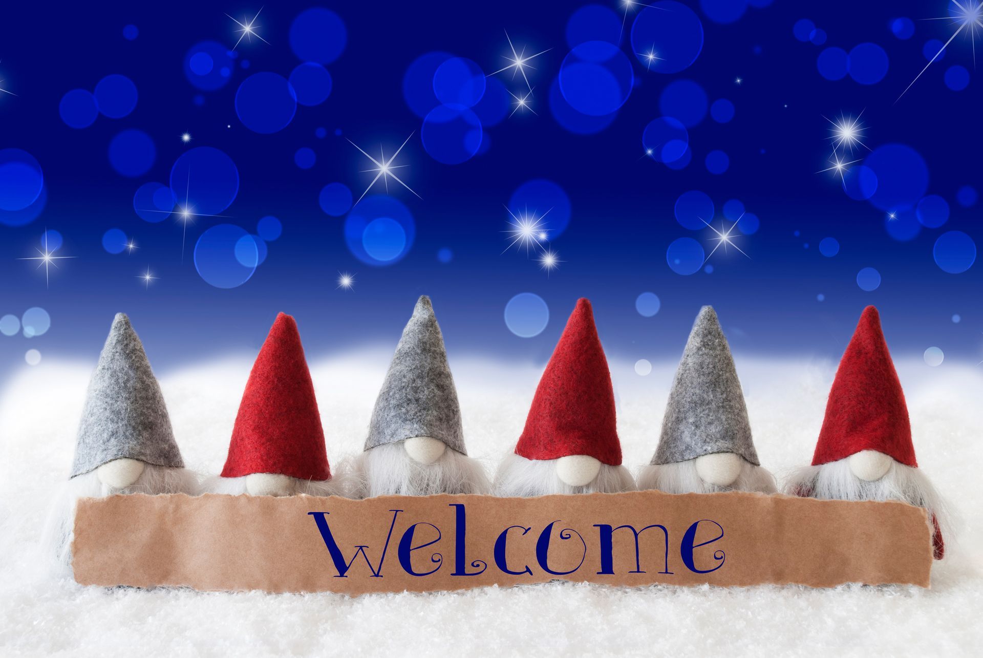 A row of gnomes sitting on top of a welcome sign in the snow.