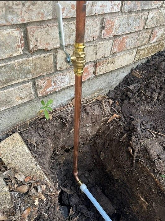 A copper pipe is sitting in the dirt next to a brick wall.