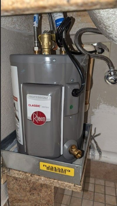 A rheem water heater is under a sink in a bathroom.