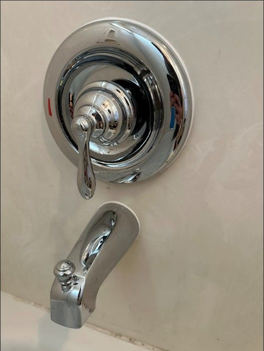 A close up of a chrome bathtub faucet on a white wall