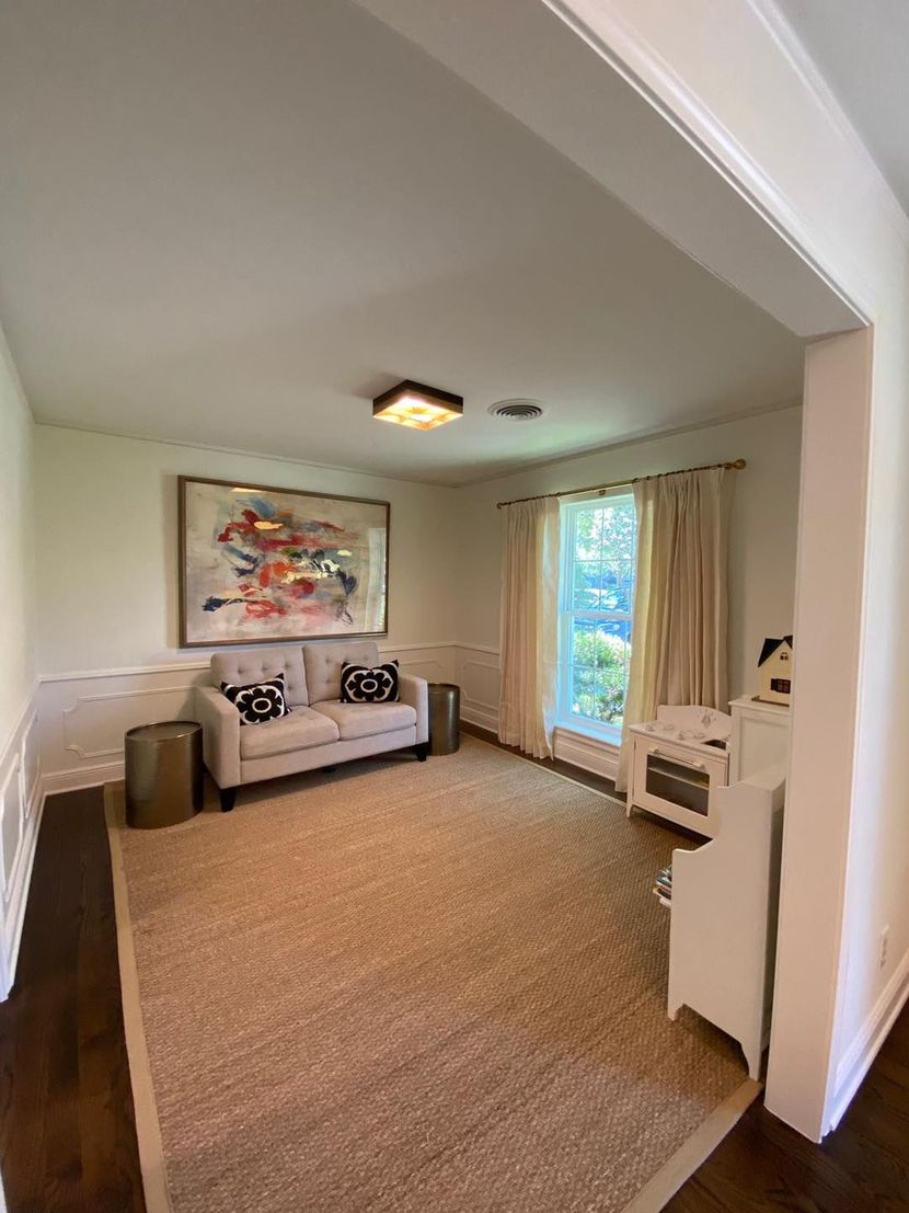 A cozy living room with a beige sofa, patterned pillows, a large abstract painting, and a neutral area rug.