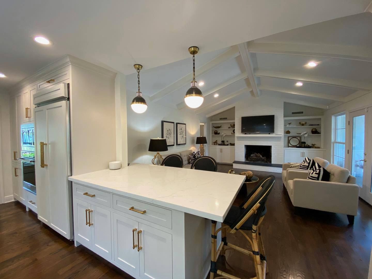 A bright open-concept kitchen with a white island and gold hardware, overlooking a living area with a fireplace.