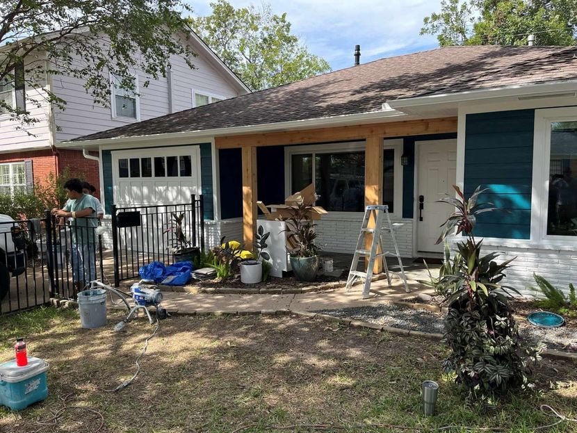 A person stands by a gated house entrance during a renovation, featuring raw wood porch posts and a blue painted wall.