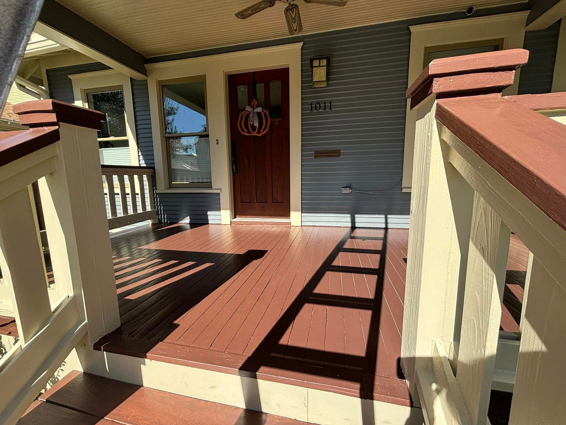 A view from front porch steps looking up toward a dark red front door, blue siding, and white railings on a sunny day.