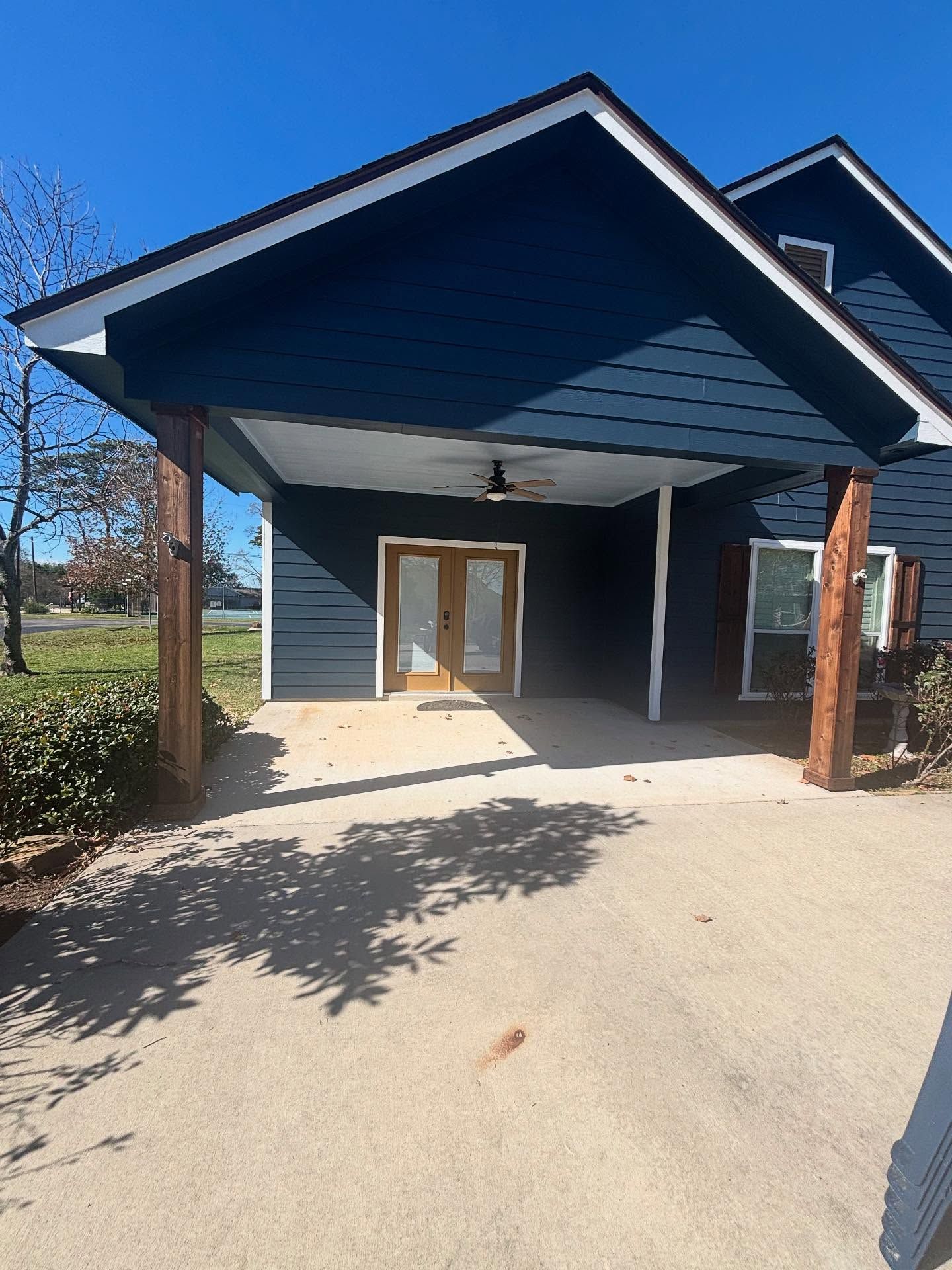 A dark blue house exterior with a covered entryway, wooden support posts, a ceiling fan, and double glass doors.