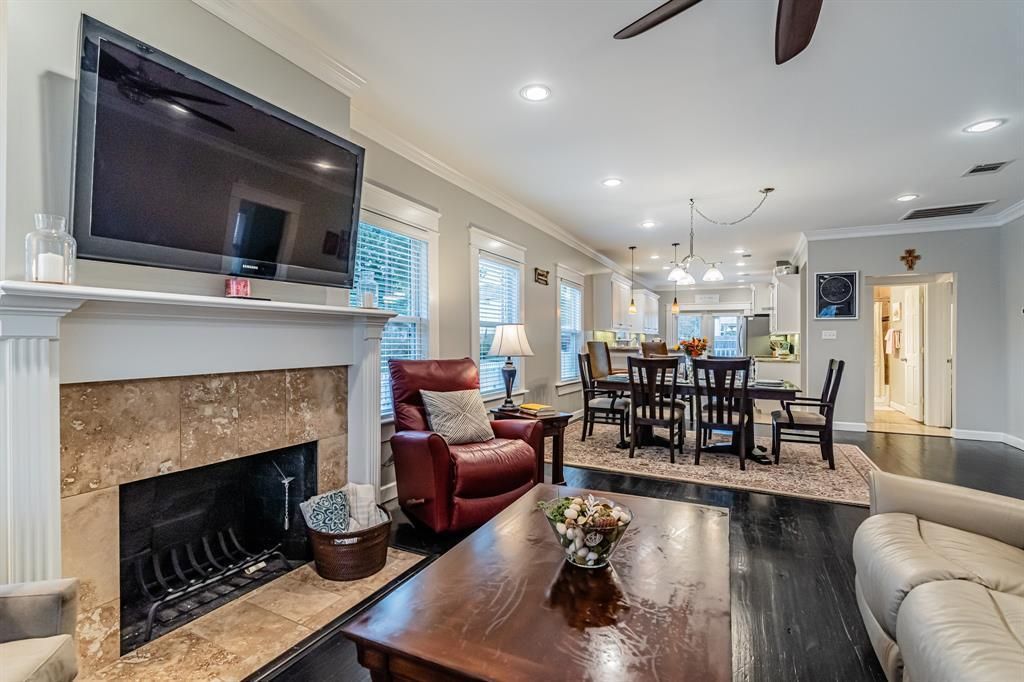 A living room with a fireplace, television, leather armchair, wooden coffee table, and an open dining area beyond.