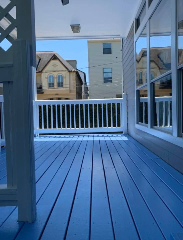 A view from a bright blue painted porch looking out through a white railing at neighboring residential houses.