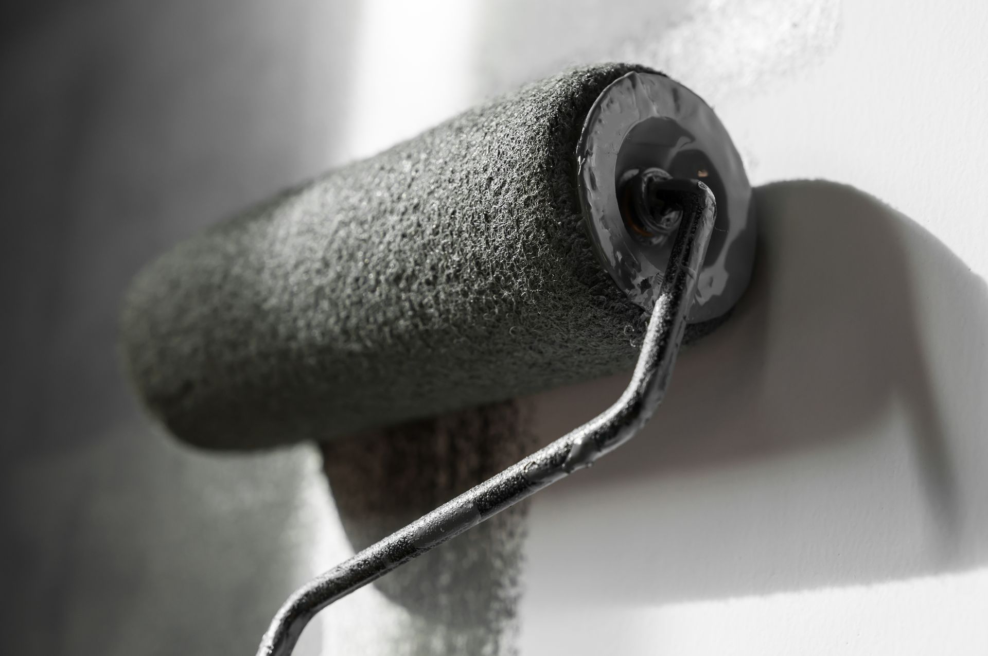 Paint roller applying dark paint to a white wall