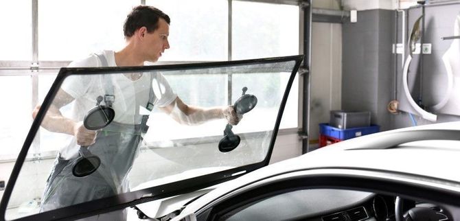 Person cleaning a car window with a squeegee in an auto shop