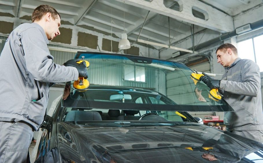 Two mechanics using power tools to repair a car windshield in a garage