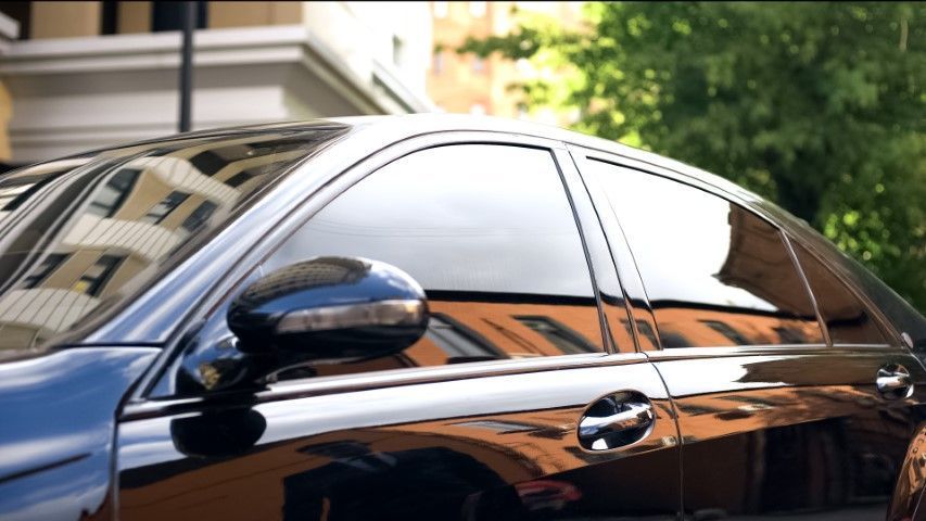 Black car side window and mirror reflecting buildings on a city street