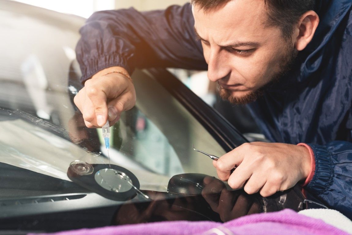 Technician using a tool to repair a car windshield, close-up in an auto shop