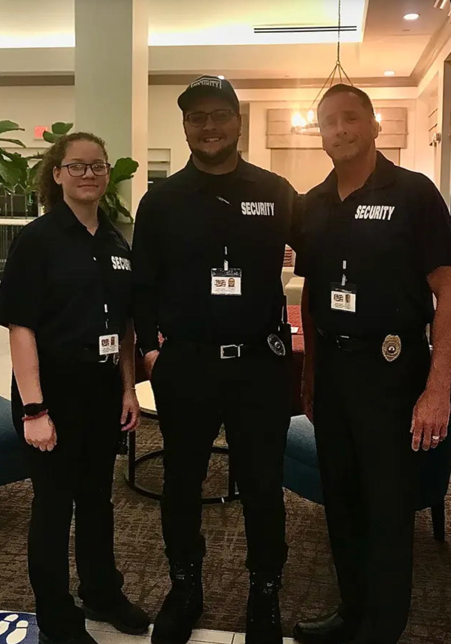 Three security guards in black uniforms pose indoors.