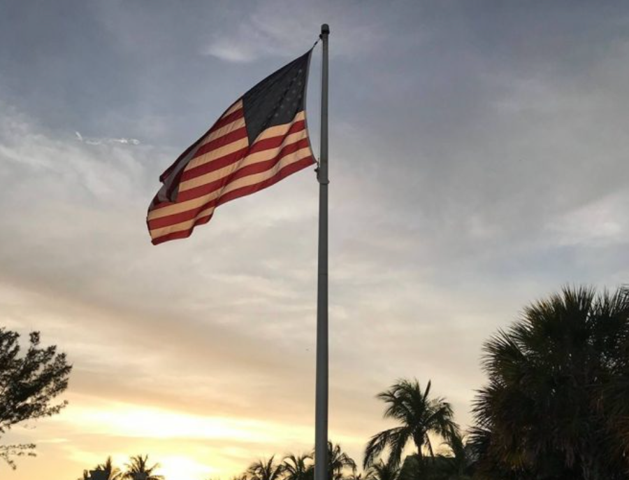 American flag waving on a tall pole against a cloudy sky at sunset.