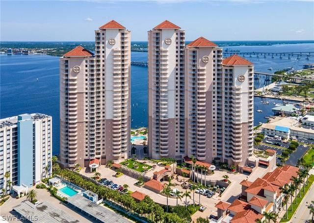 High-rise condos with red tile roofs and tan exteriors, near a river and bridge.
