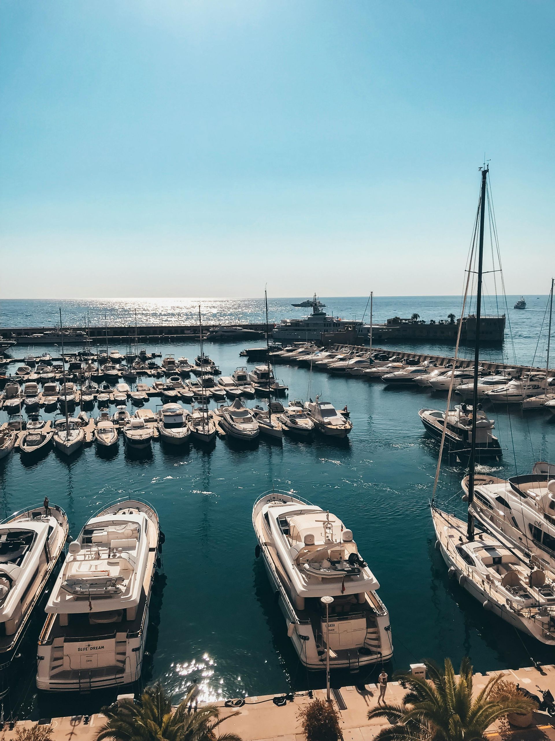 Boats docked in harbor, turquoise water, sunny sky.