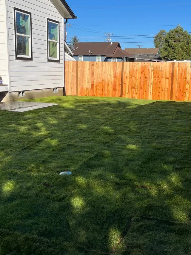 A backyard with a wooden fence and a house in the background.