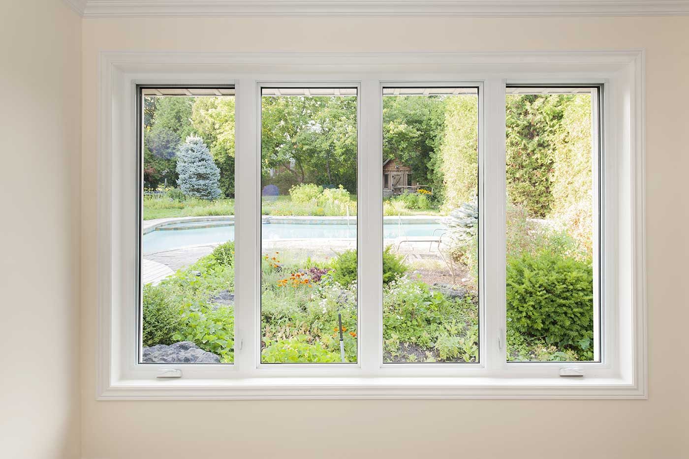 A large white window with a view of a garden and a pool.