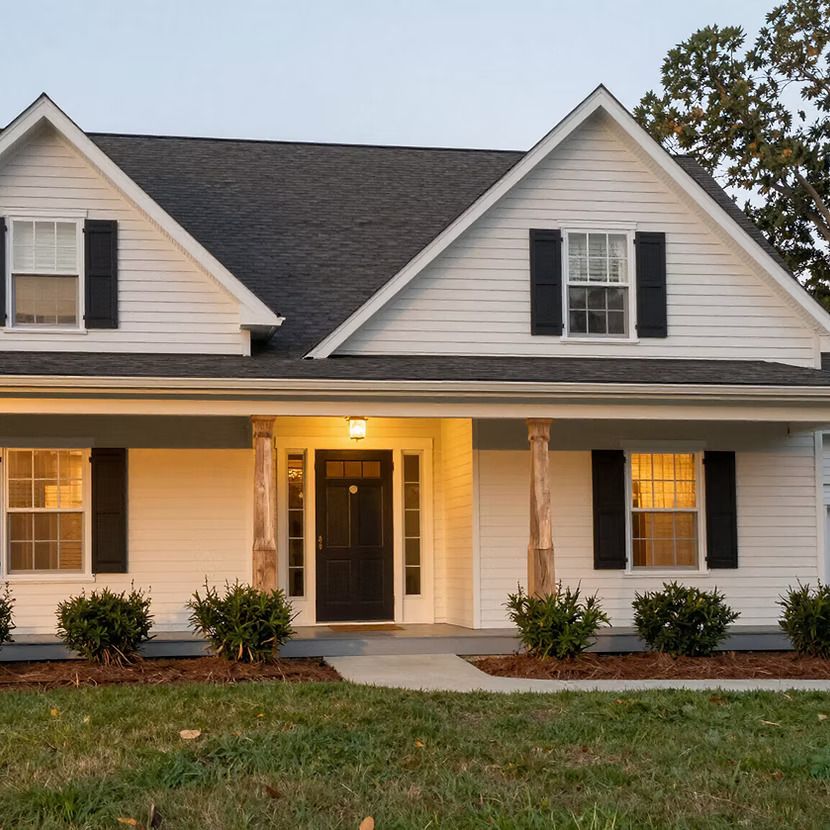 Suburban house exterior at dusk with lit porch and white siding