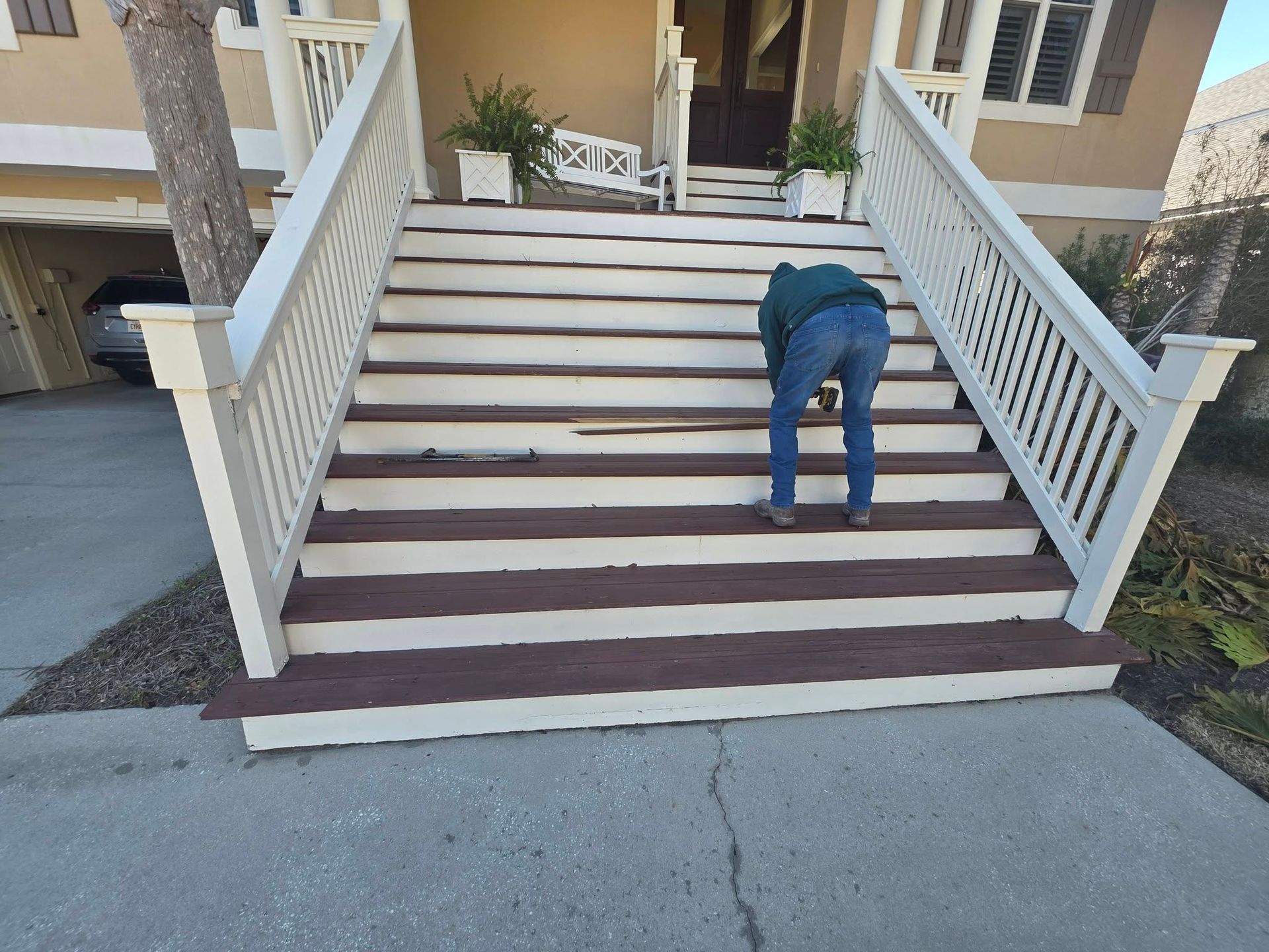 Person bent over on outdoor stairs in front of a building, near a white railing.