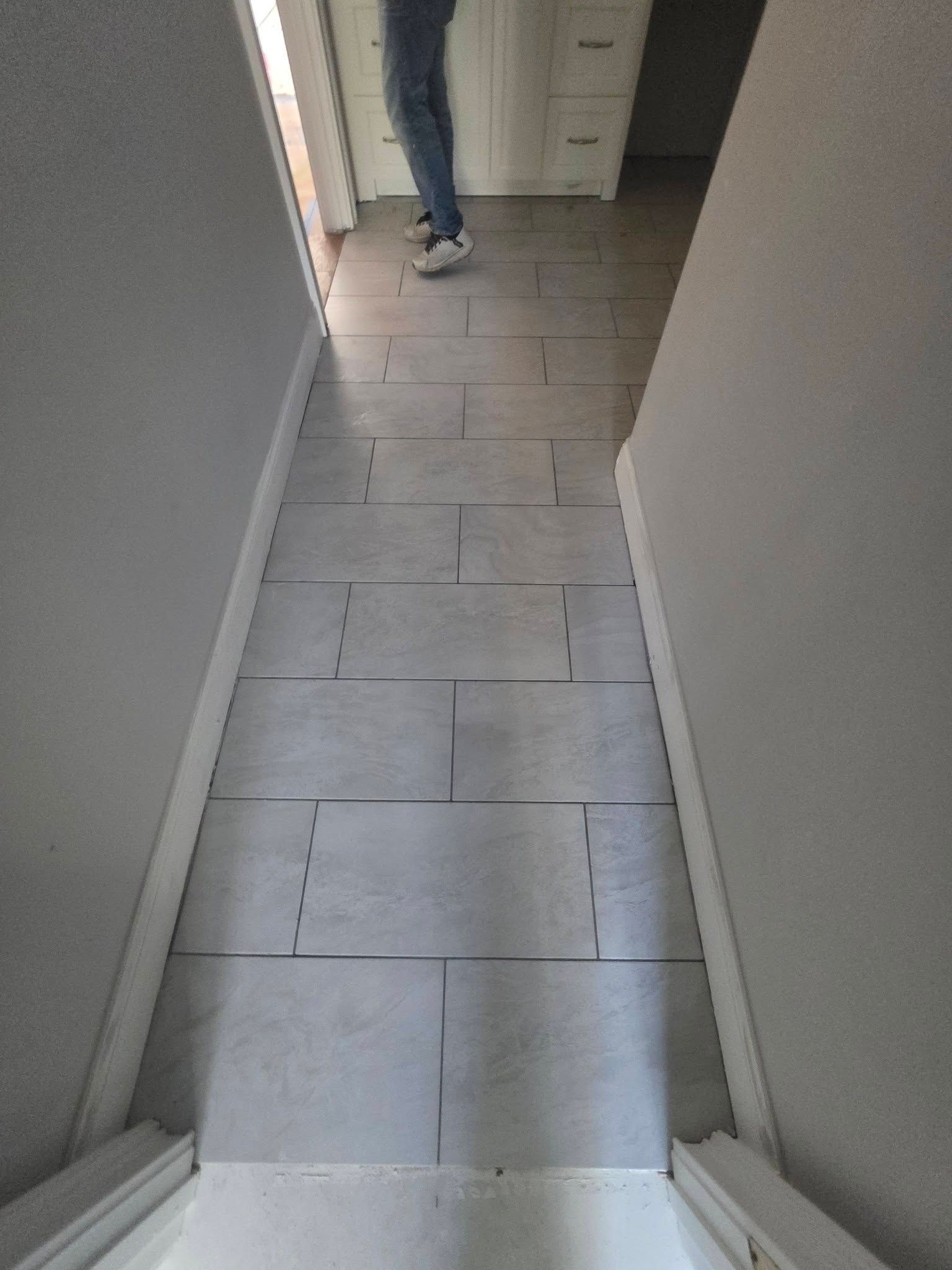 Narrow hallway with light tile floor and a person standing near a doorway at the far end