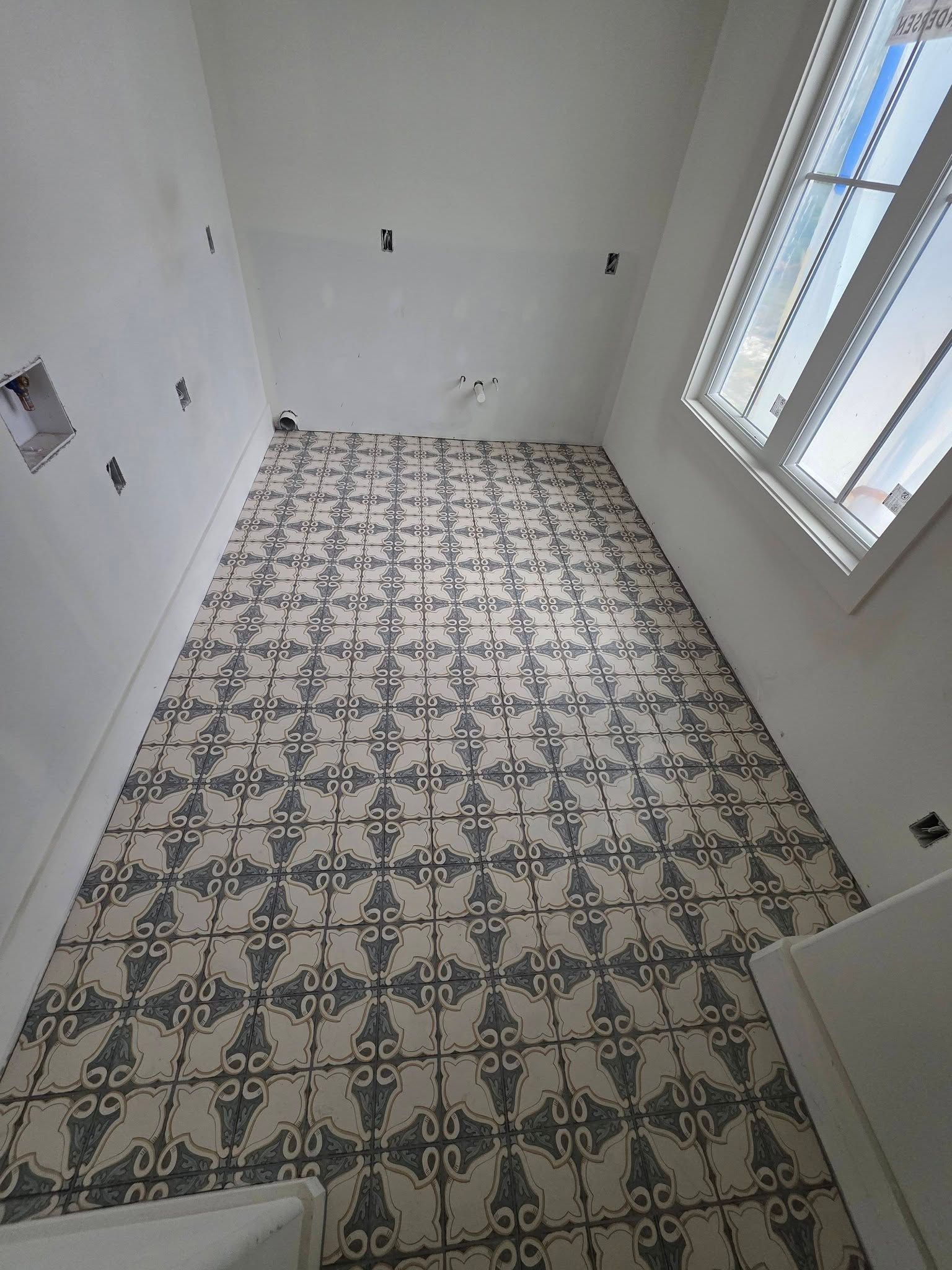 Empty tiled room with white walls and a window, viewed from the doorway.