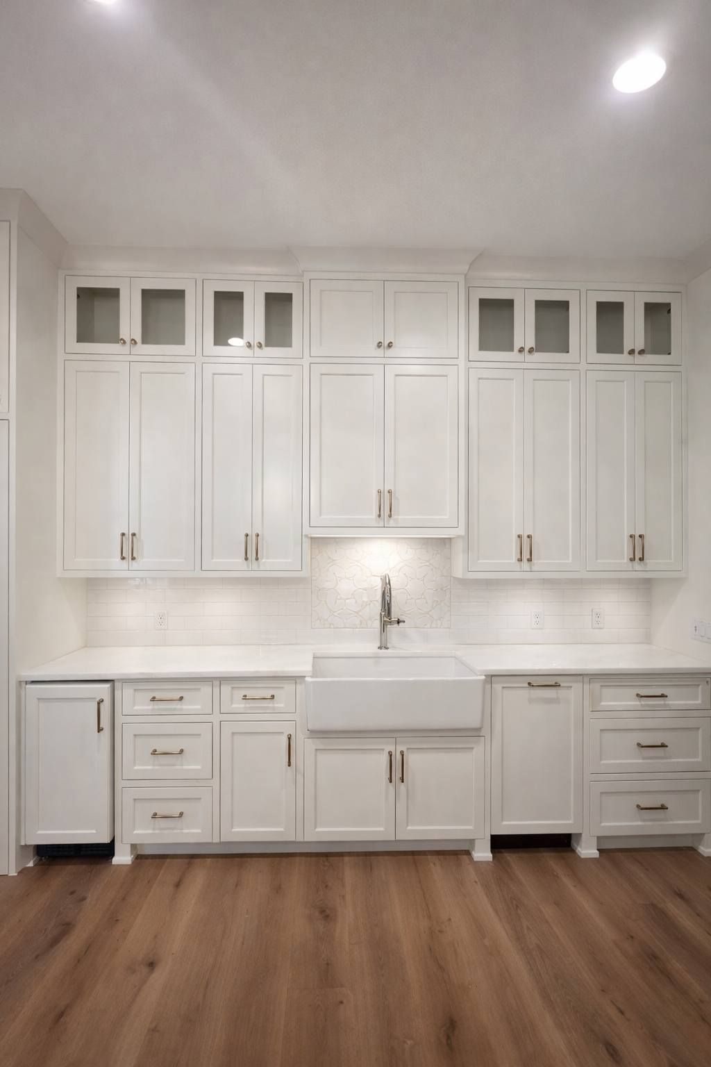 White laundry room with sink, cabinets, and wood floor under bright recessed lighting