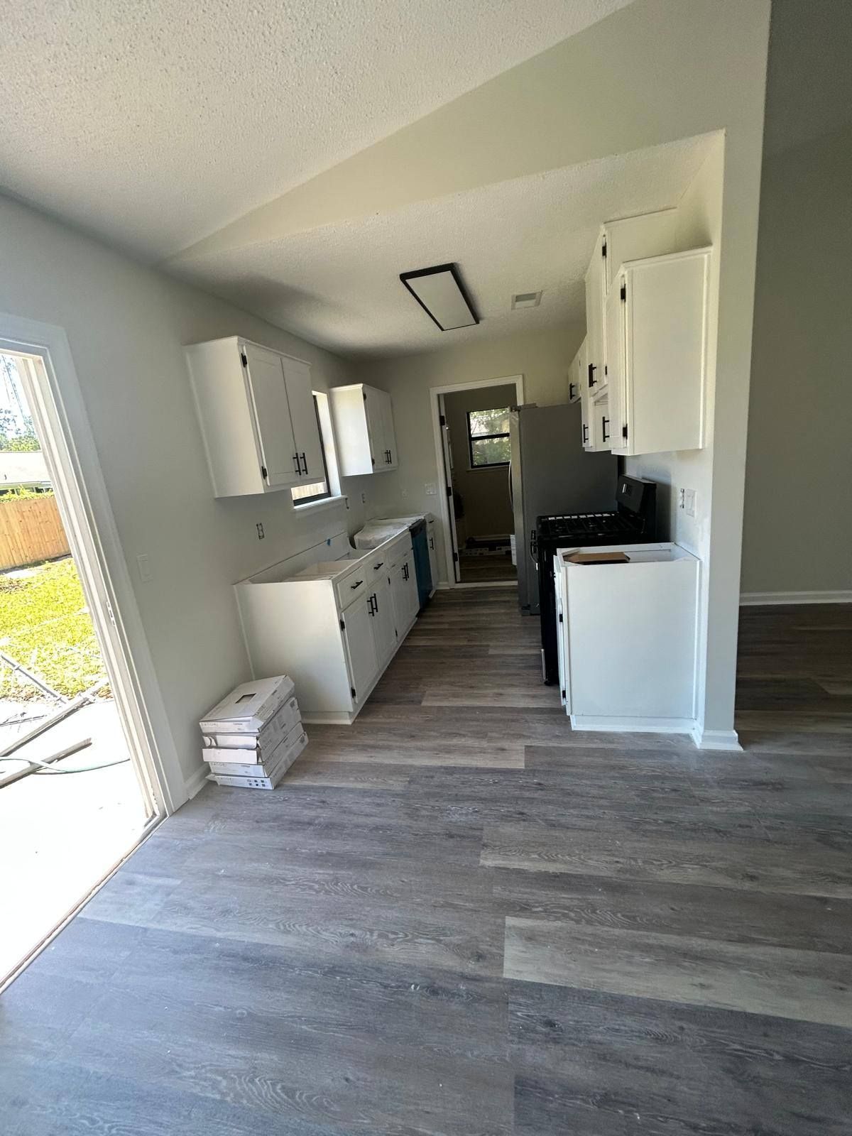Bright kitchen interior with white cabinets, gray flooring, and a doorway to a hallway.