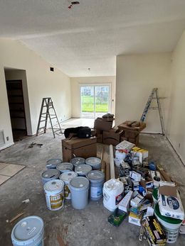 Unfinished room with paint supplies, ladders, boxes, and buckets of paint on the floor.